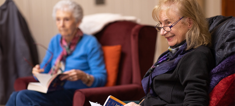 Two elderly women seated near each other enjoying their own activities