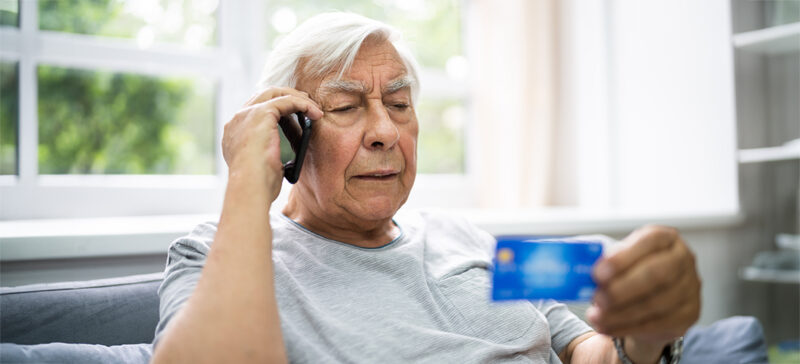 elderly person holding phone to ear with credit card in other hand