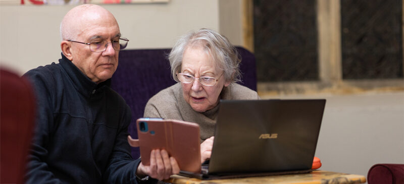 elderly couple looking at a phone and a laptop
