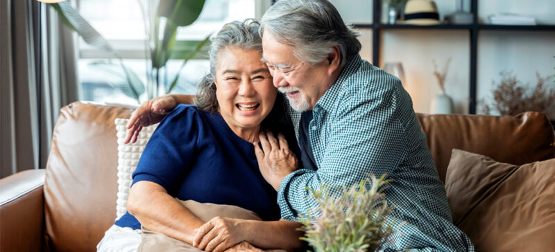 older adult couple seated on a couch together smiling