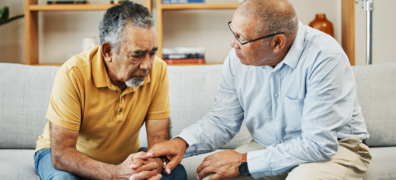two elderly men seated together on a couch seeming concerned