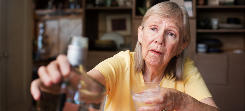 older woman holding a bottle of alcohol and a glass