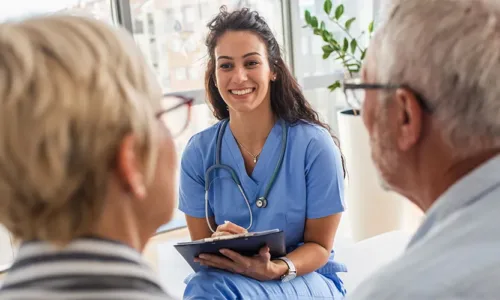 healthcare working holding a clipboard with elderly couple in foreground