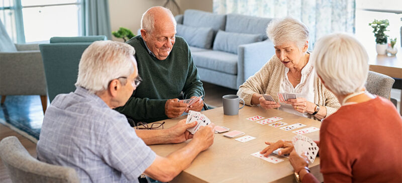 4 elderly people seated around a table with cards laid out