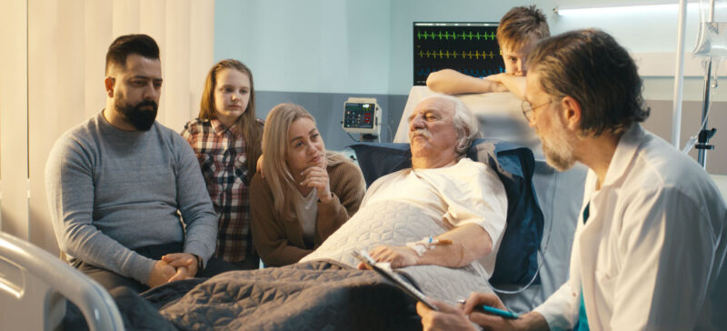 older adult in hospital bed surrounded by concerned family members