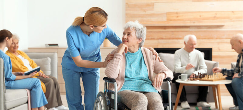 older adult woman in wheelchair with younger healthcare worker leaning in to speak with her