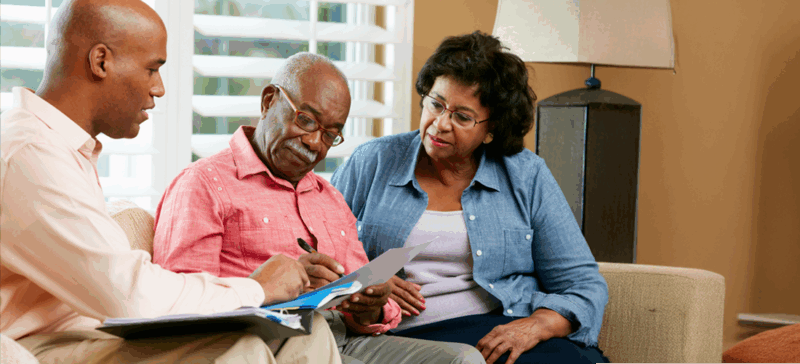older adult gentleman seated on couch between younger man and woman looking over papers