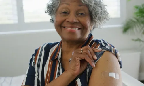 smiling, older adult woman with her shirt sleeve rolled up, showing a band aid from a vaccine.