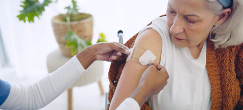 older adult woman looking at arm as medical professional applies a post vaccine band-aid
