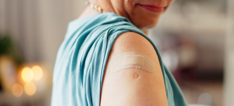 smiling, older adult woman with sleeve rolled up and band-aid on arm