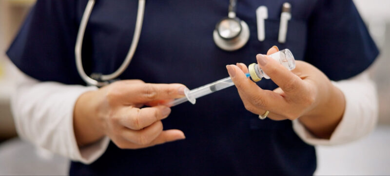 closeup of medical professional holding vaccination vial and needle